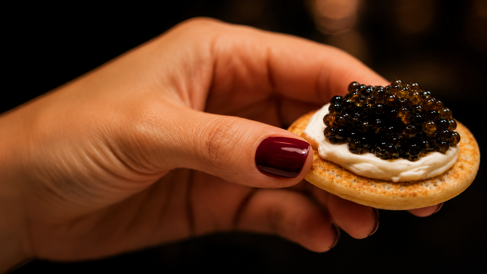 Main féminine tenant un blini, crème fraîche et caviar